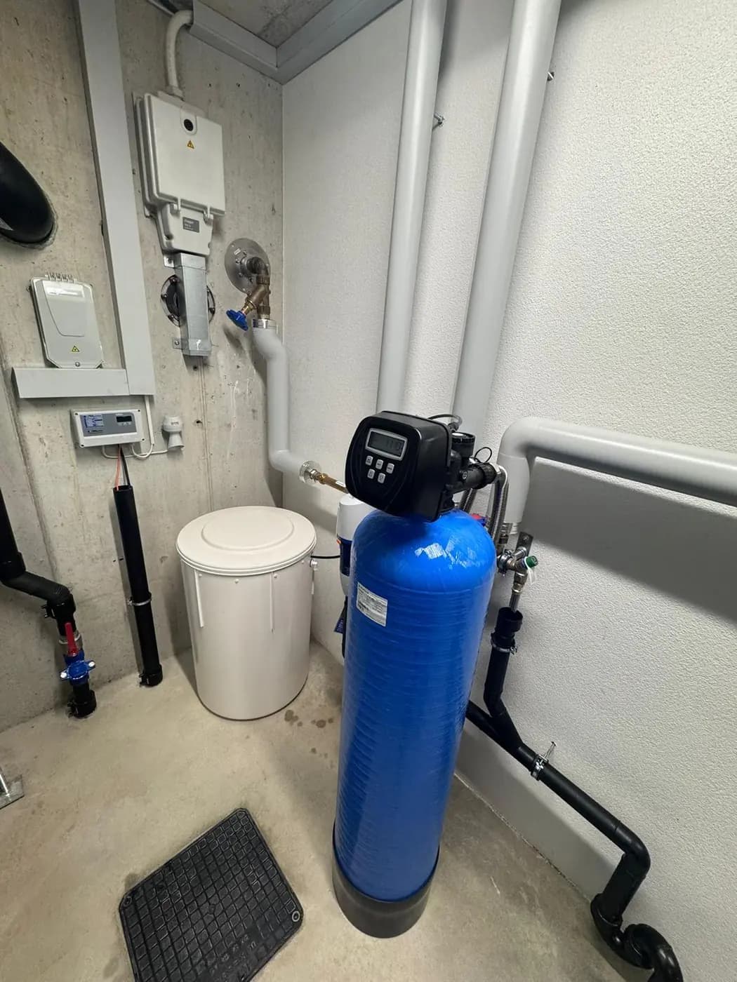 Enthärtungsanlage mit blauem Ionenaustauscher-Drucktank, Steuerkopf und Salzbehälter im Technikraum eines Mehrfamilienhauses in Oberentfelden